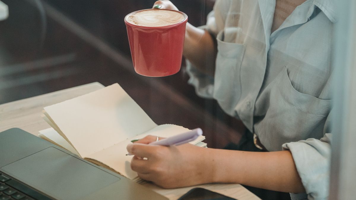 コーヒーを片手にノートに書き込んでいる手元のイメージ
