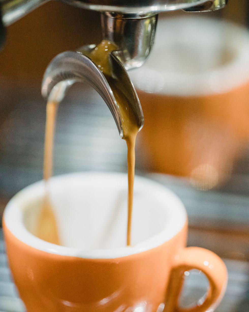 Espresso streaming from the machine into a small ceramic cup