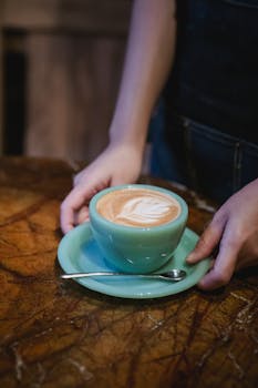 Close-up of a woman holding a blue cup with latte art on a wooden table.