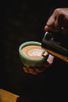 A barista pouring exquisite latte art into a coffee cup in a dimly lit café.