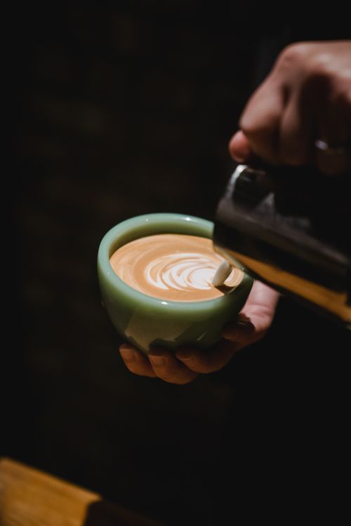 Free A barista pouring exquisite latte art into a coffee cup in a dimly lit café. Stock Photo
