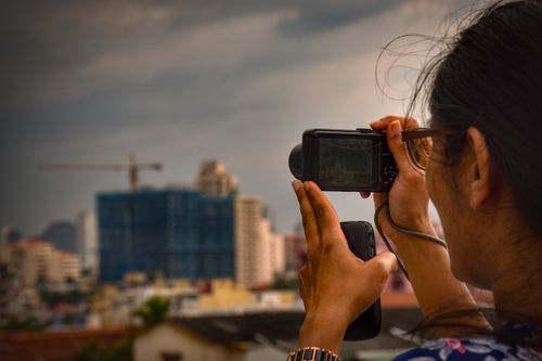 Free A woman uses a camera to photograph a city skyline at dusk, capturing urban development. Stock Photo