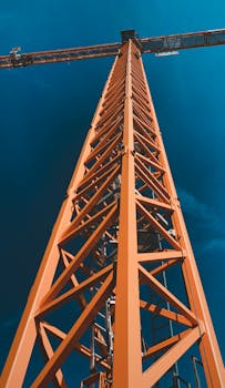 Low angle view of an orange tower crane against a clear blue sky in Alkmaar, Netherlands.