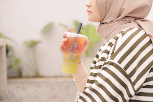 Free Woman in Brown Hijab Holding Orange Juice in Clear Plastic Cup Stock Photo