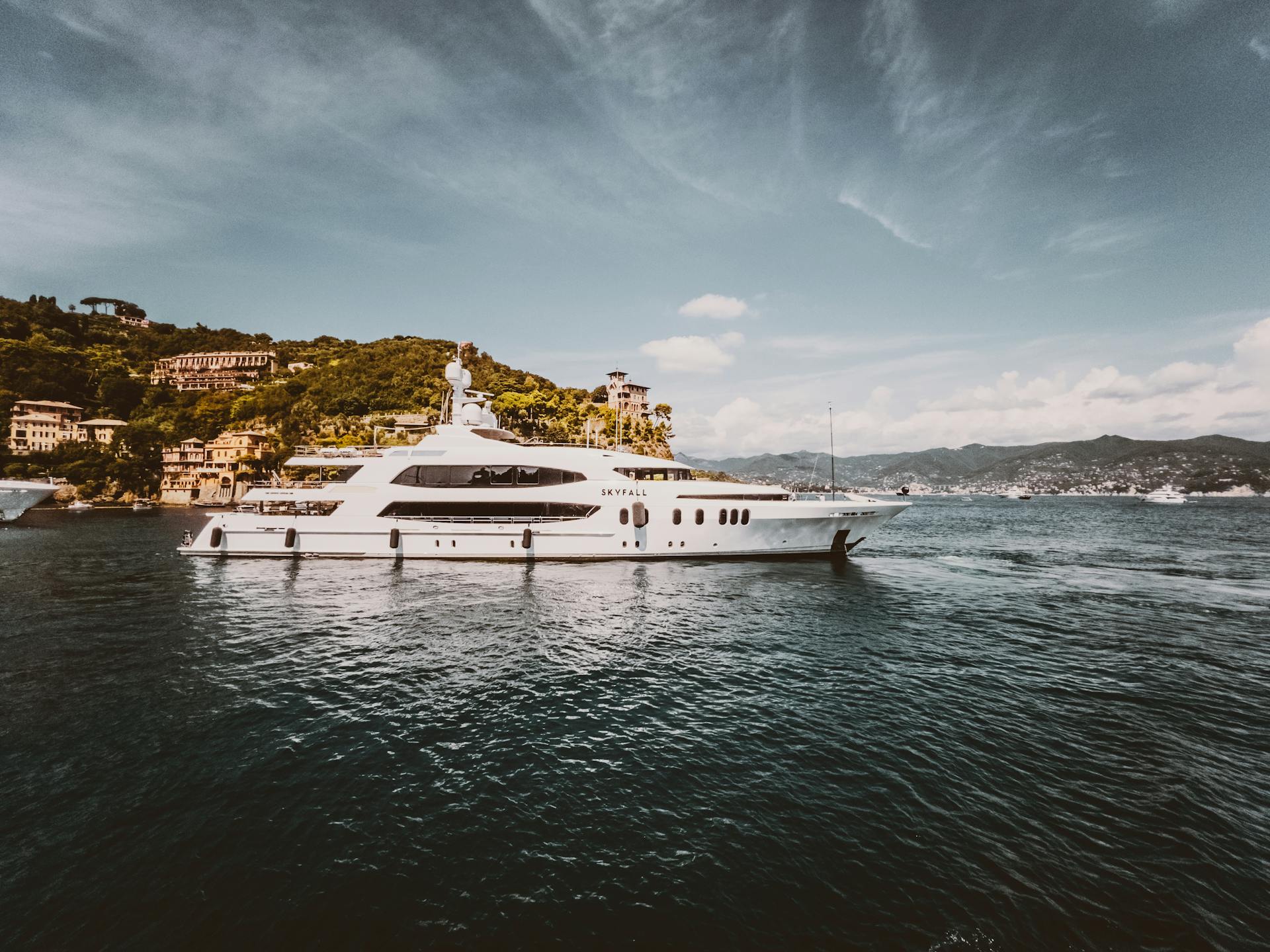 Elegant yacht cruising near the lush, scenic shores of an Italian coastal town under a clear blue sky.