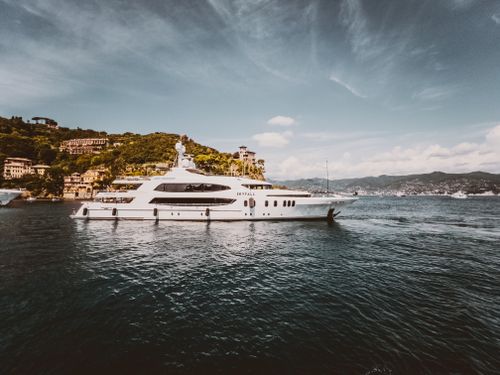 Free Elegant yacht cruising near the lush, scenic shores of an Italian coastal town under a clear blue sky. Stock Photo