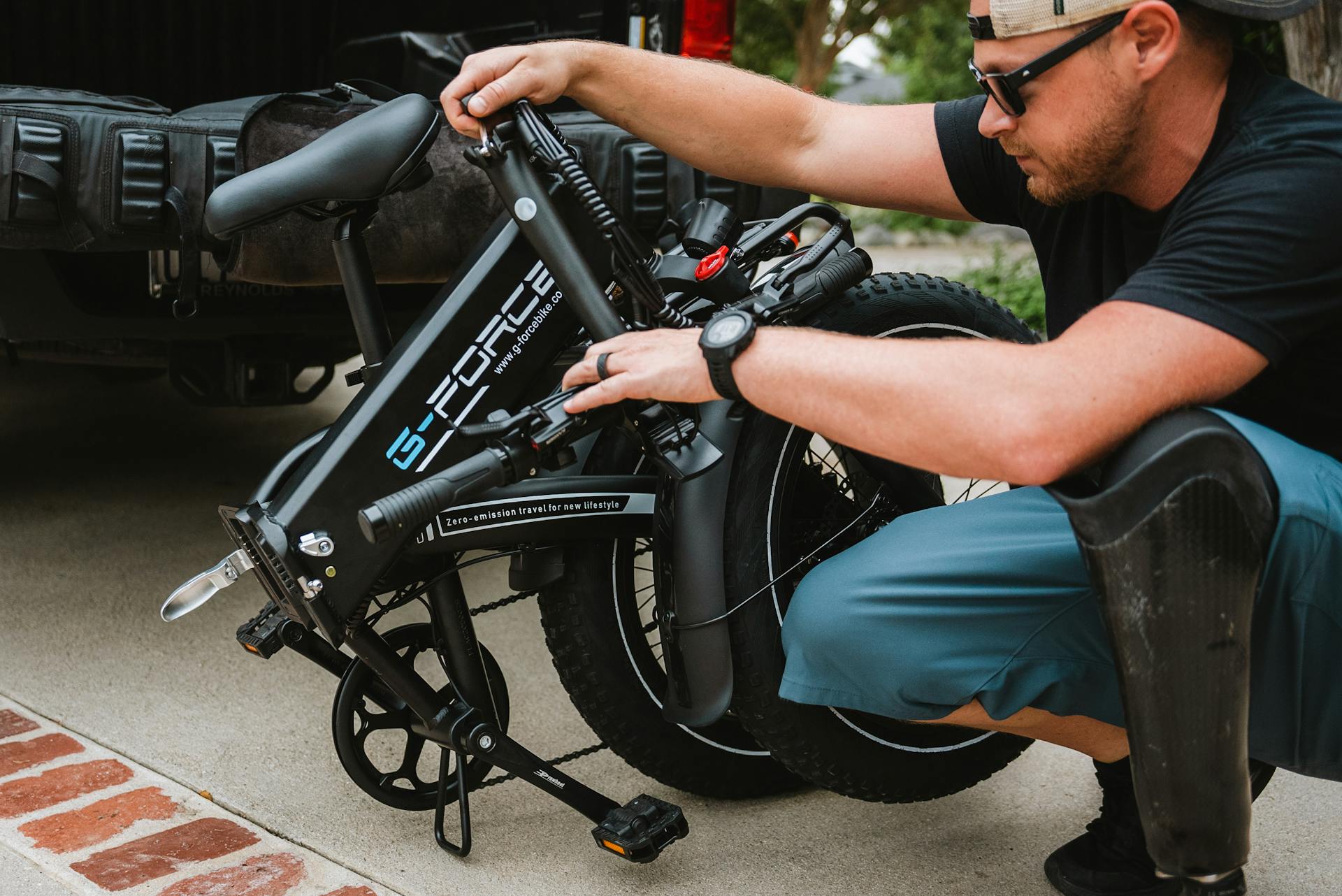 A man folds a G-Force electric bike next to a truck, emphasizing outdoor lifestyle and convenience.