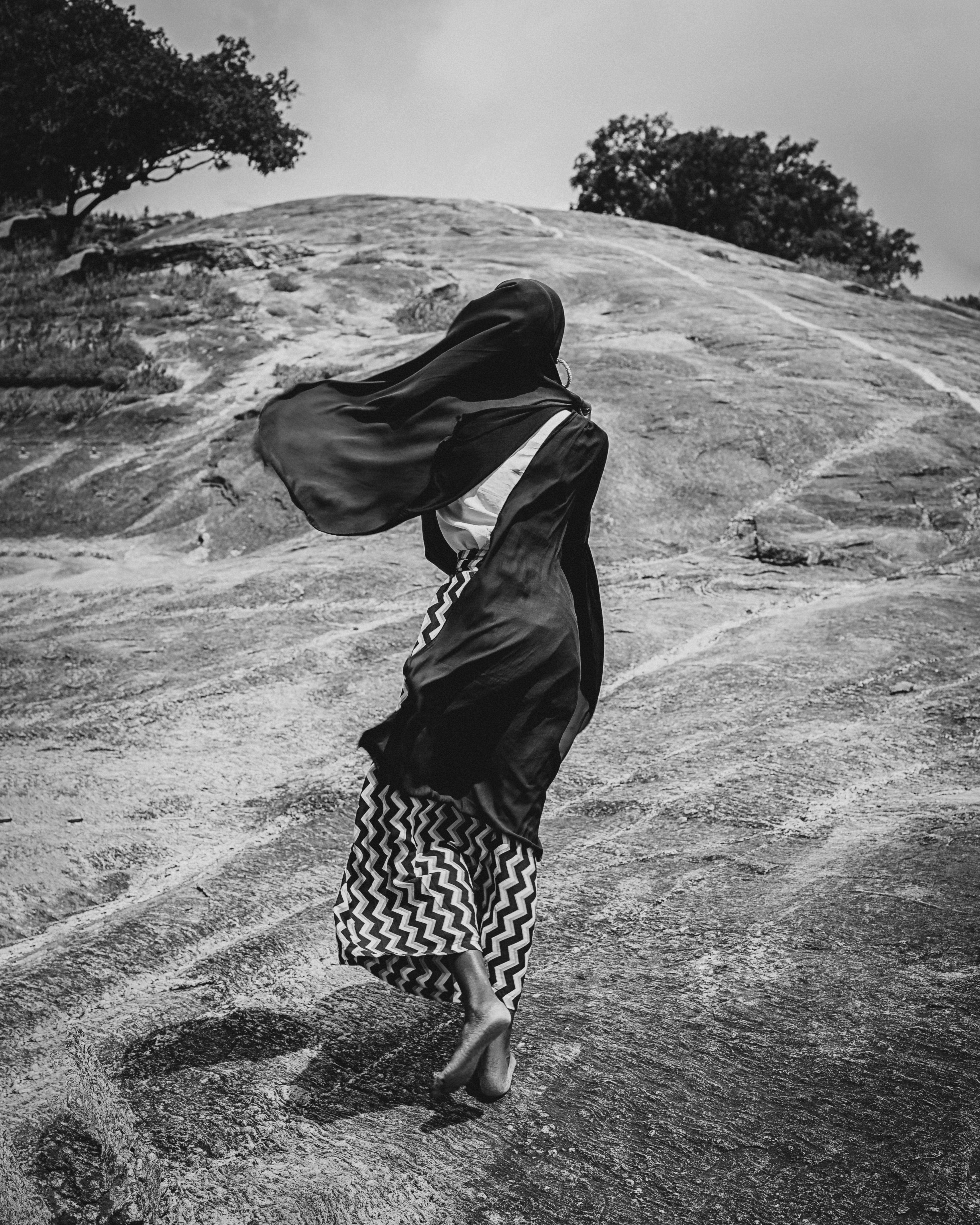 A woman in a black dress walks barefoot on a rocky hill in Ilorin, Nigeria.