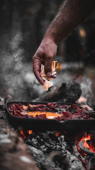 Close-up of hand adding ingredients to pan over firewood flames in Istanbul outdoors.