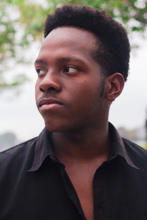 Free Close-up portrait of a young man outdoors, looking pensive with a natural background. Stock Photo