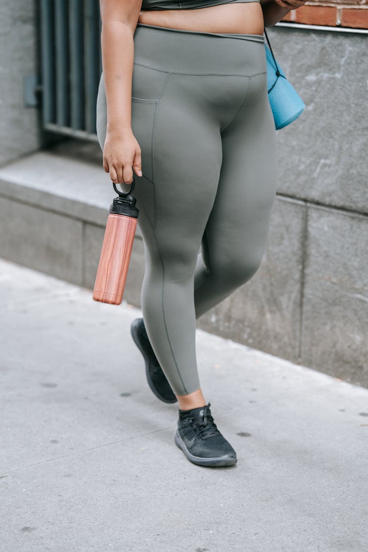 Woman Walking In Sport Clothing Carrying A Yoga Mat And A Water Bottle 