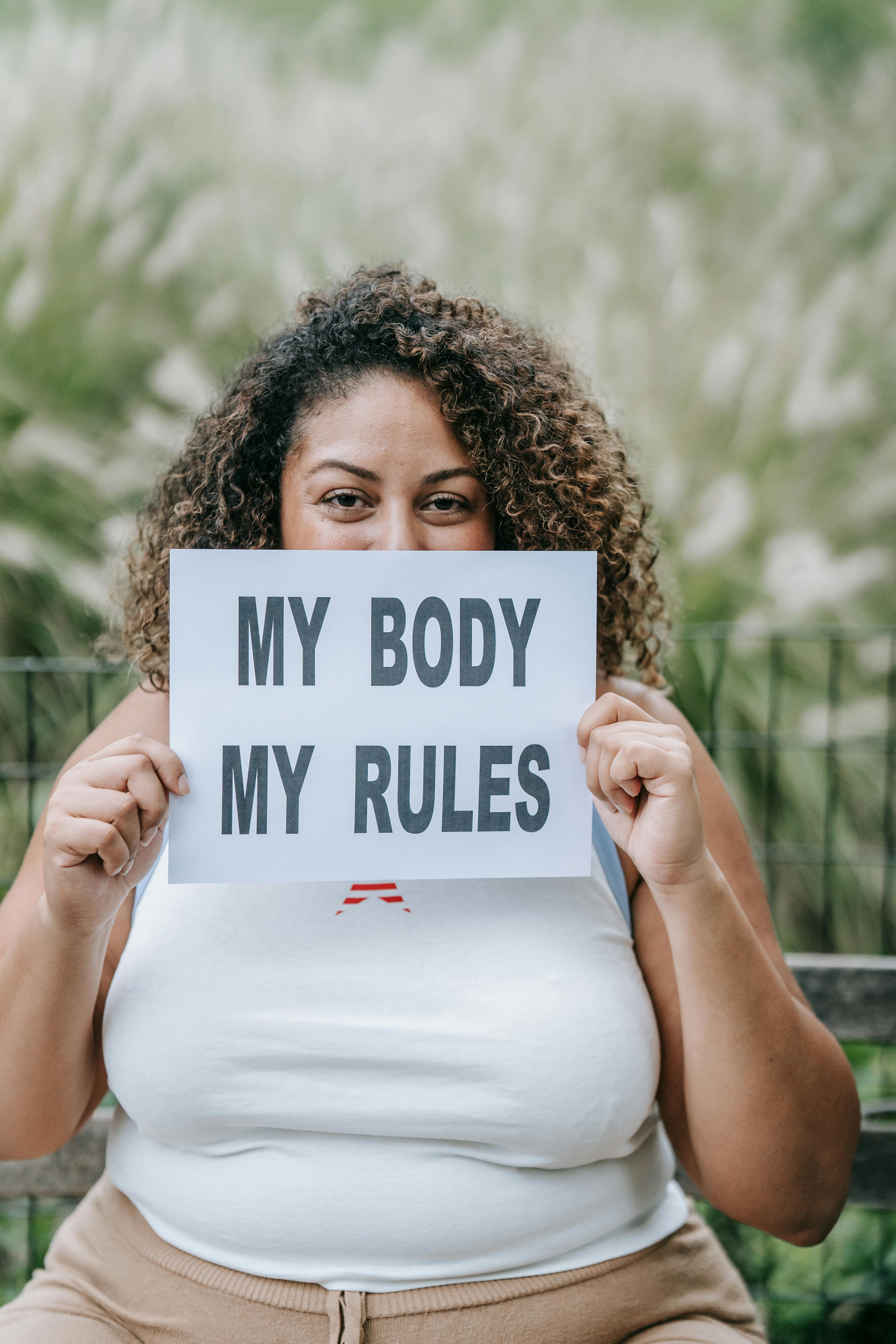 woman holding paper with my body my rules written on it