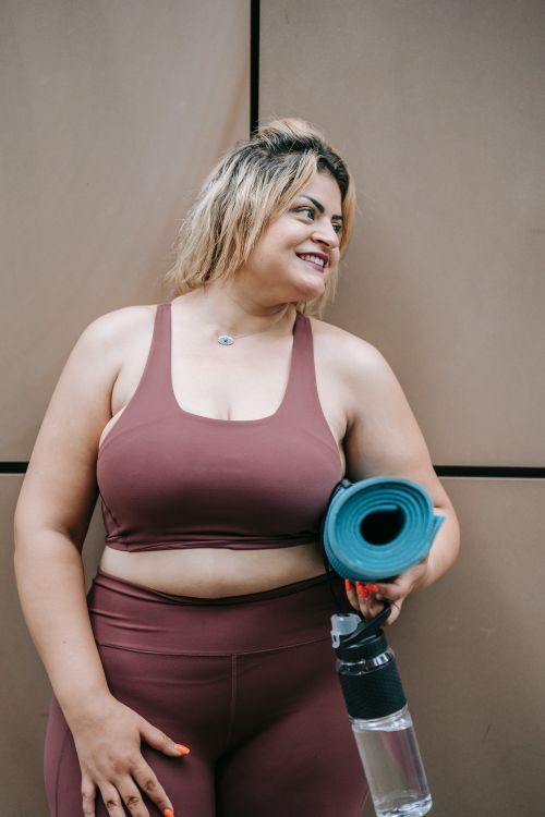 Free Smiling woman in sports attire holding a yoga mat and water bottle, ready for workout. Stock Photo