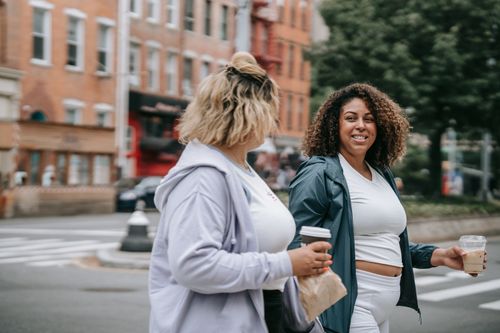 Free Two women walking in urban setting with drinks, enjoying casual conversation. Stock Photo