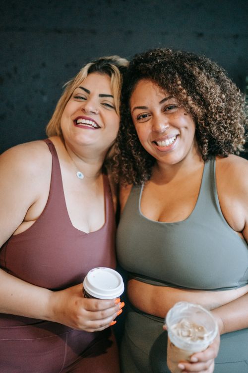 Free Two women in activewear smiling and enjoying coffee together indoors. Stock Photo
