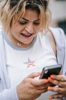 A woman with blonde hair using a smartphone outdoors while smiling.
