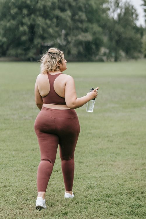 Free Rear view of a woman walking in a park holding a water bottle. Stock Photo