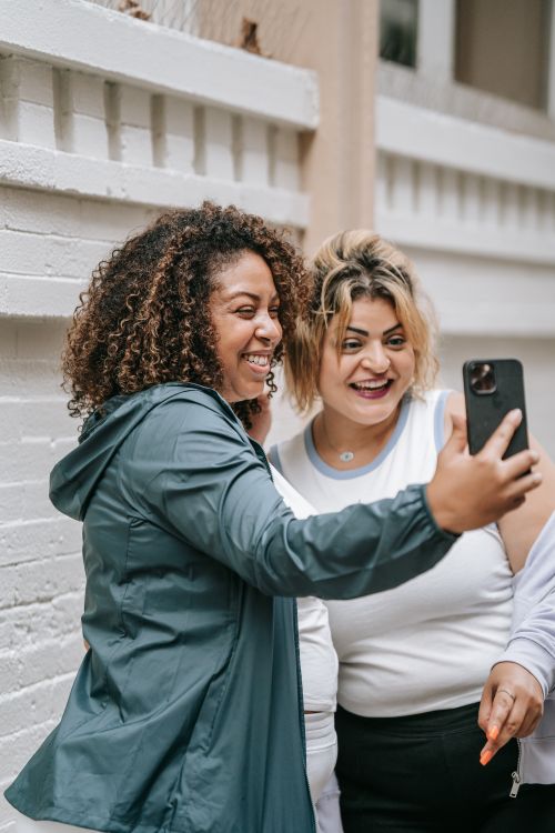 Free Two women taking a cheerful selfie outdoors against a brick wall. Stock Photo