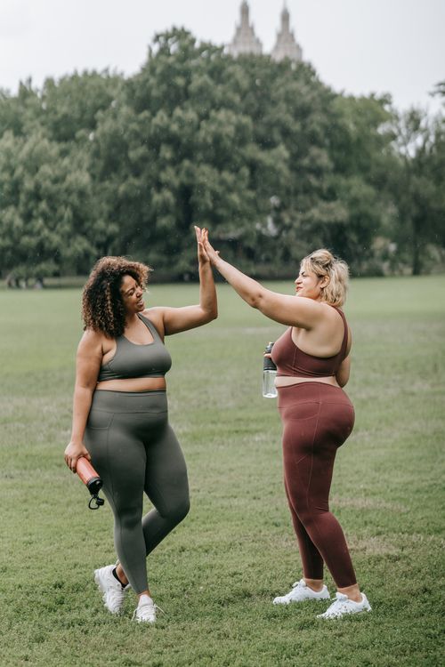 Free Two women in sportswear celebrate with a high five during a workout in a grassy park. Stock Photo
