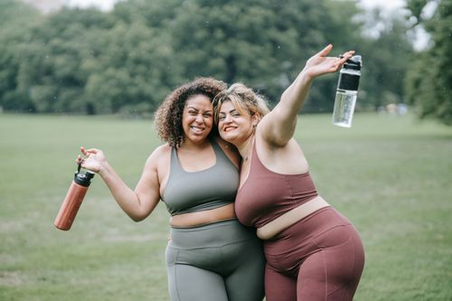Free Two women in sportswear smiling and hugging outdoors, holding water bottles. Stock Photo
