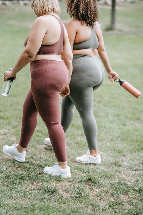 Free Two women walking on grass in sports clothing, holding water bottles. Focus on fitness and outdoor exercise. Stock Photo