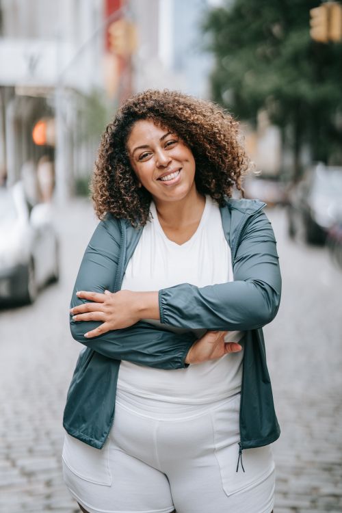 Free A woman with curly hair smiling confidently while standing on a cobblestone street in the city. Stock Photo