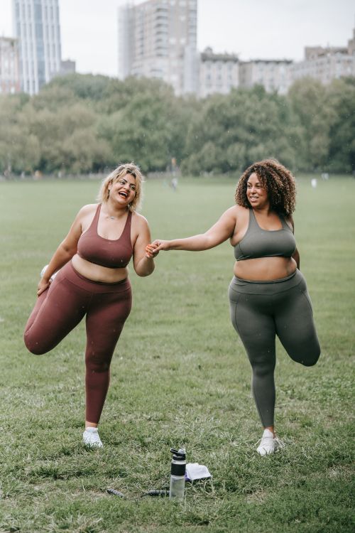 Free Two women stretching together in a park, smiling and enjoying their workout. Stock Photo