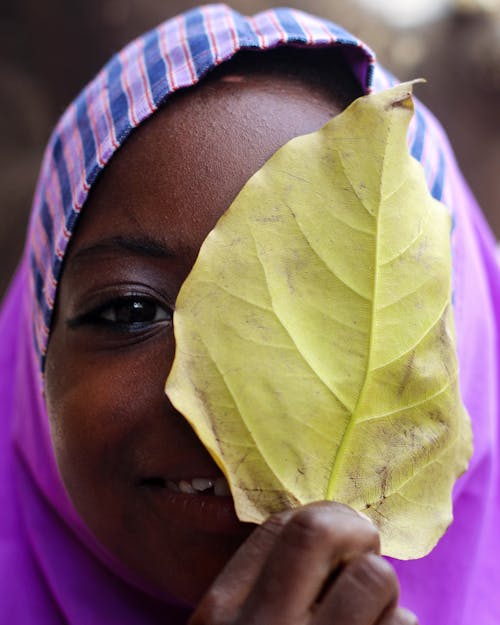 A Hijab Woman Covering Her Face With a Yellow Leaf