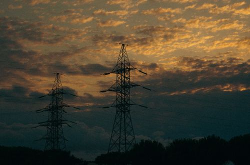 Free Silhouetted electric towers with dramatic sunset and dark cloudscape, emphasizing industrial technology. Stock Photo