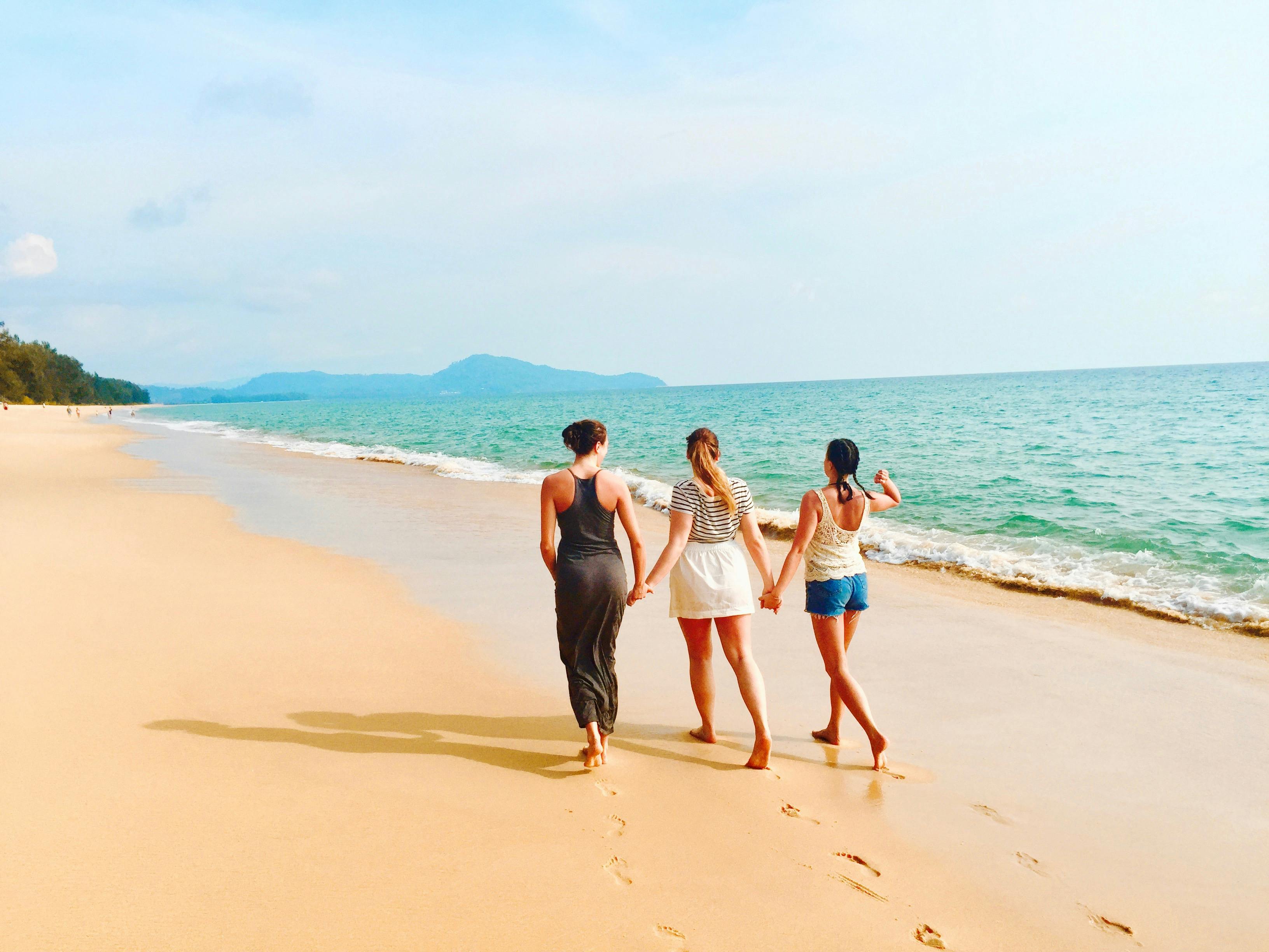 three women walking on seashore under blue sky