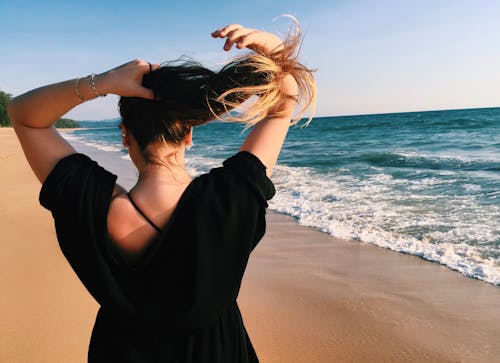 Woman Holding Her Hair While Standing Beside Shoreline