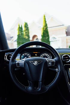 Interior view of a luxury car focusing on the steering wheel with a house in the background.