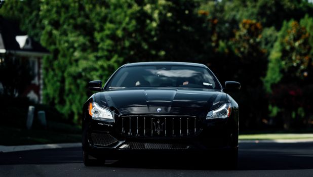 A luxurious black car parked outdoors under sunlight, front view.