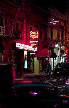 Neon-lit street view of downtown San Francisco at night with cars and signs.
