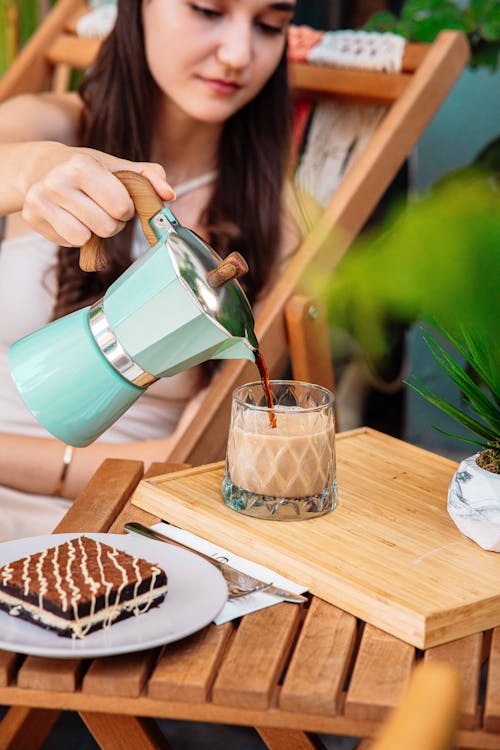 Woman Sitting on a Deck Chair Pouring Coffee from a Percolator