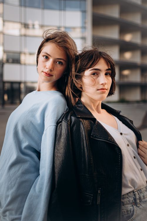 Free Two young women posing back to back outdoors, showcasing fashion and confidence in a city setting. Stock Photo
