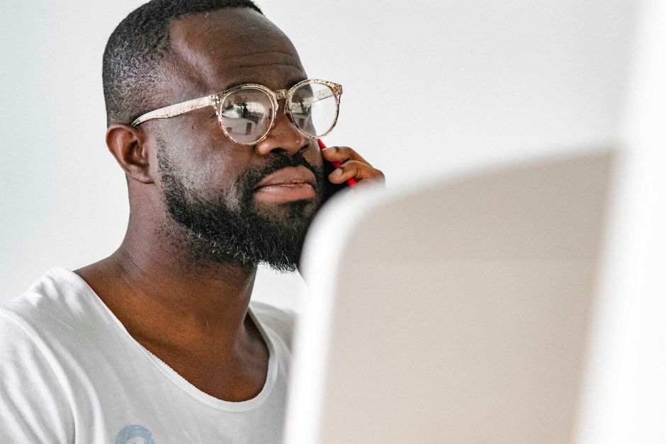 A young man with glasses making a phone call indoors, exhibiting focus and communication.