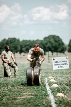 Soldiers engage in a military training exercise involving a road-wheel rolling task outdoors.
