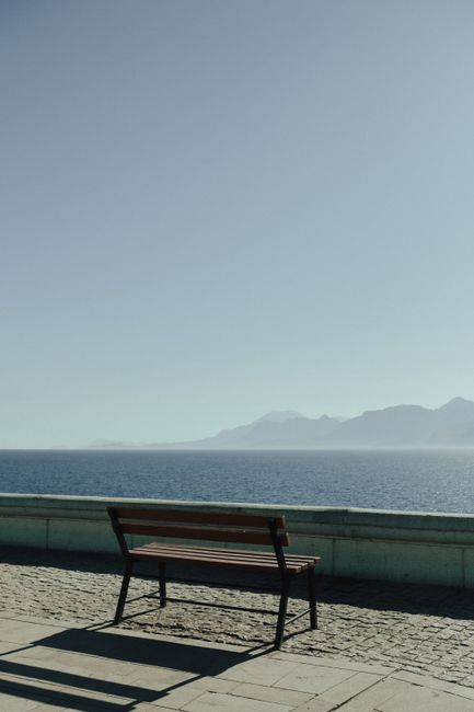 A peaceful scene of a solitary bench overlooking a calm sea with clear skies.