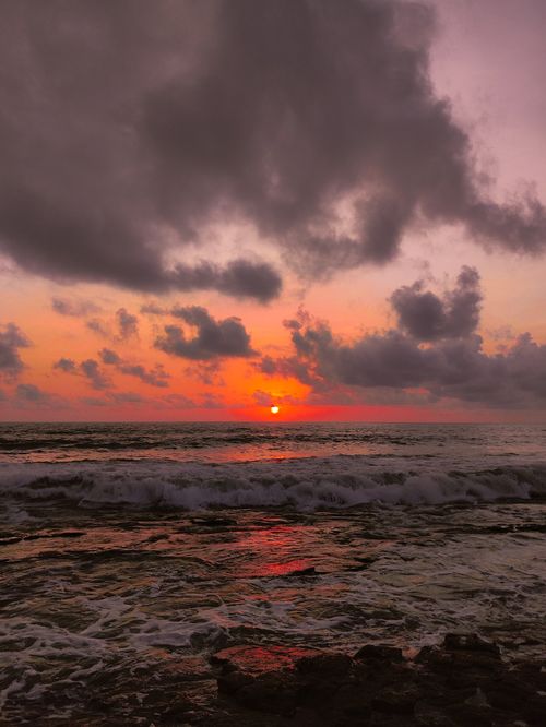 Free Capture of a breathtaking sunset over the ocean with waves crashing against the shore and dramatic clouds in the sky. Stock Photo
