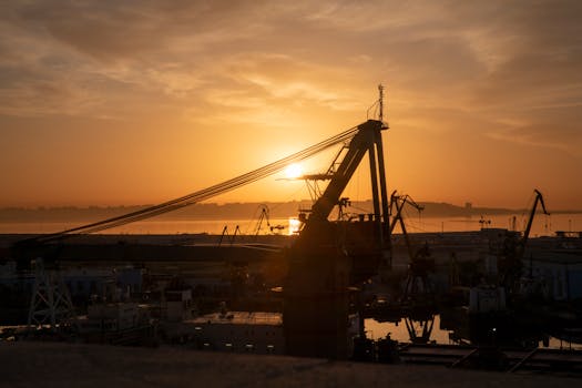 Silhouette of cranes in Baku port at sunrise, reflecting on the sea, creating a stunning industrial scene.