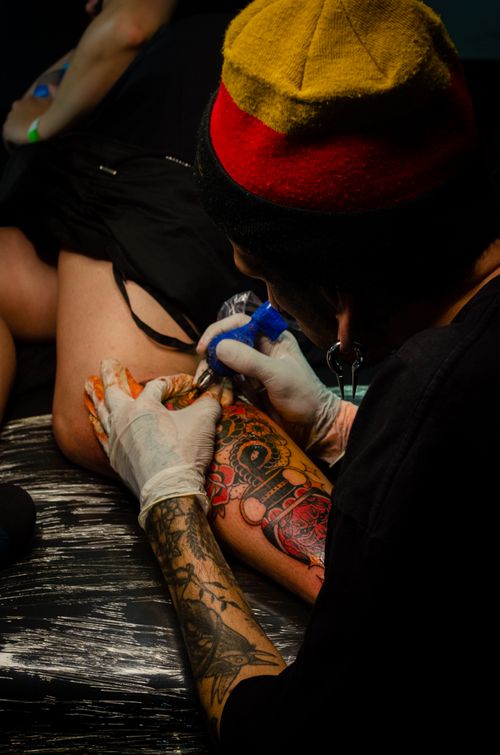 Free Close-up of a tattoo artist working on a vibrant leg tattoo in a studio setting. Stock Photo