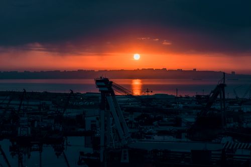 Free Stunning sunset view over Baku harbor with silhouettes of cranes and city skyline reflecting on the water. Stock Photo