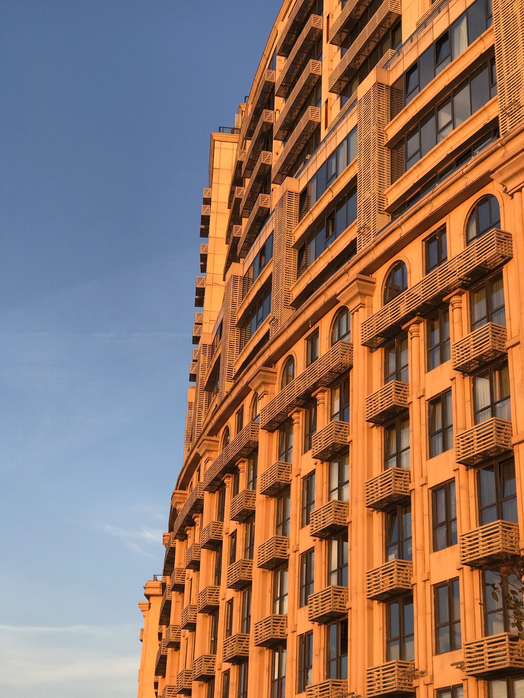 Fachada soleada de edificio residencial con hileras de ventanas y balcones.