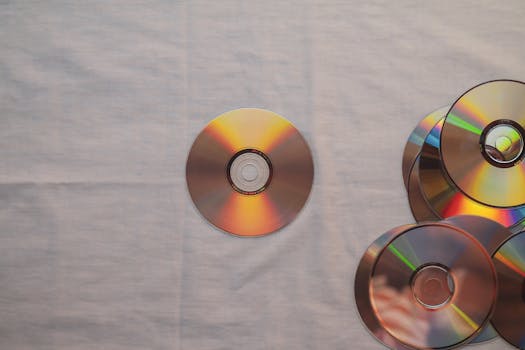 Aesthetic top view of multiple CDs with colorful reflections on a plain surface.