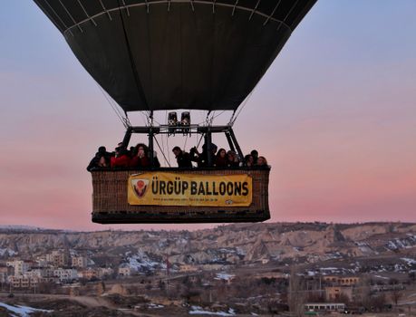 A hot air balloon carrying people soars over Cappadocia, Türkiye, at sunset.