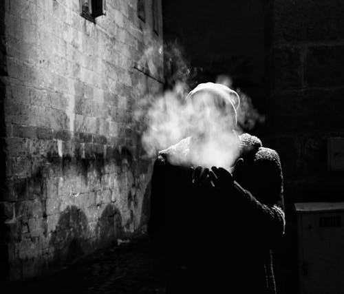 Man Standing near a Wall at Night with His Face Hidden behind Smoke 