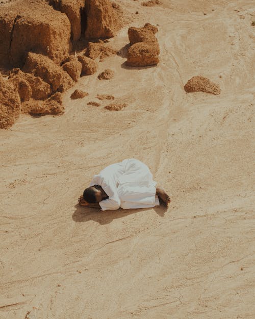Man Dressed in White Lying Curled Up on a Desert
