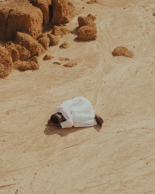 A solitary man dressed in white rests on sandy desert terrain, capturing solitude in Lagos, Nigeria.