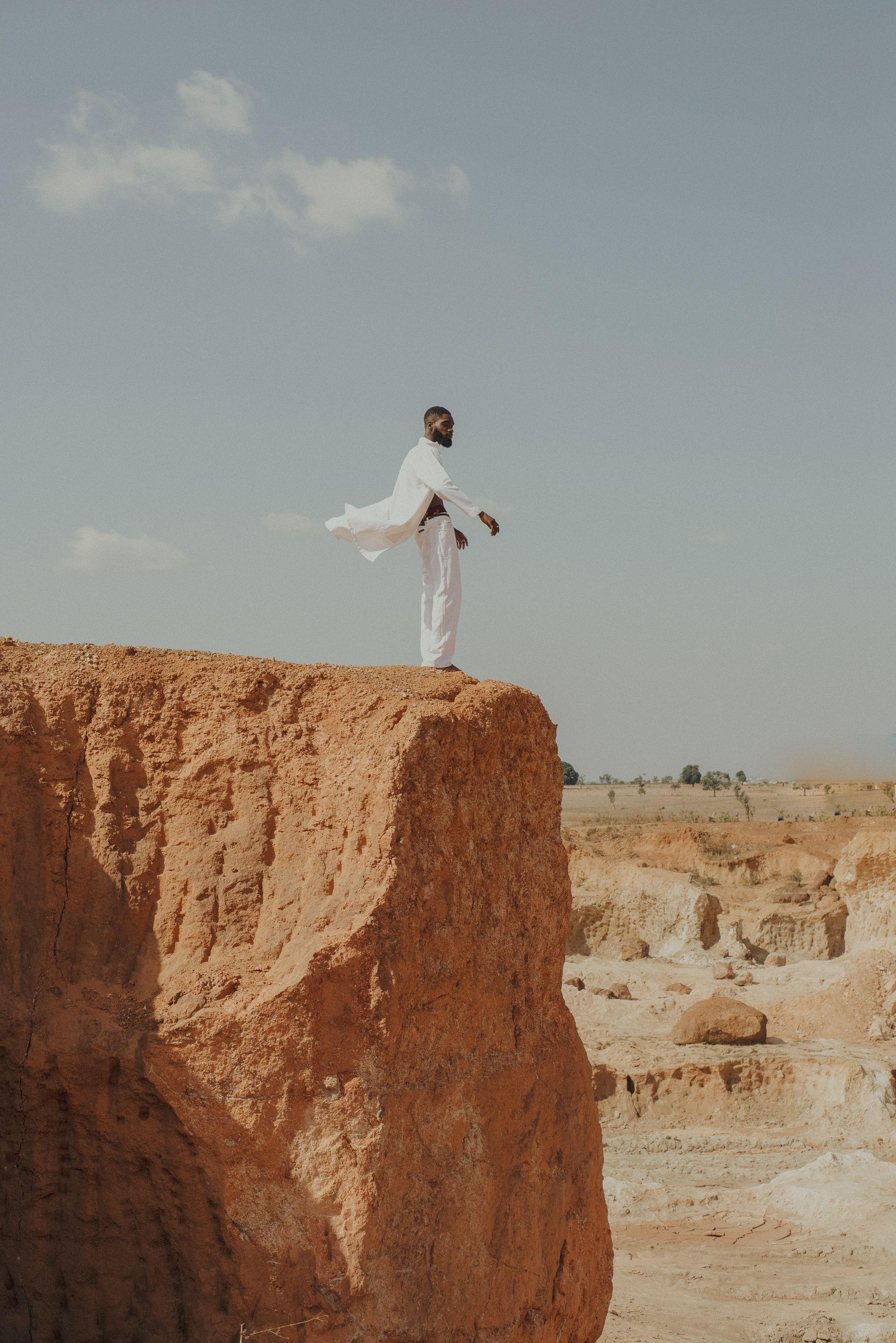 A man in a white outfit stands on a cliff edge in Lagos, capturing a desert-like landscape.